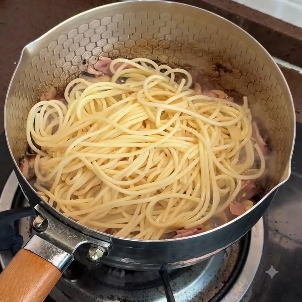 Des pâtes dans une poêle prêtes à être mélangées avec la sauce à la truffe et aux jaunes dœufs.