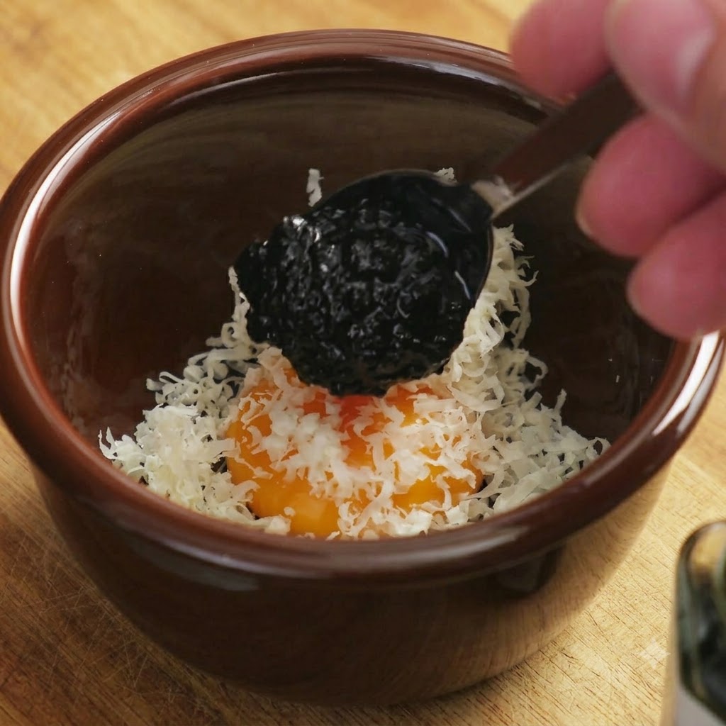 Une cuillerée sombre de sauce à la truffe noire déposée sur le mélange de jaune dœuf et de fromage.