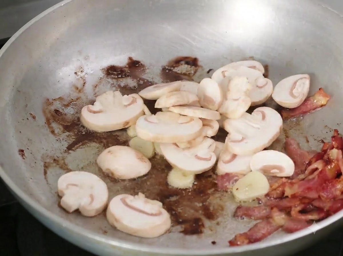 Champignons émincés ajoutés à la poêle avec le bacon et lail.