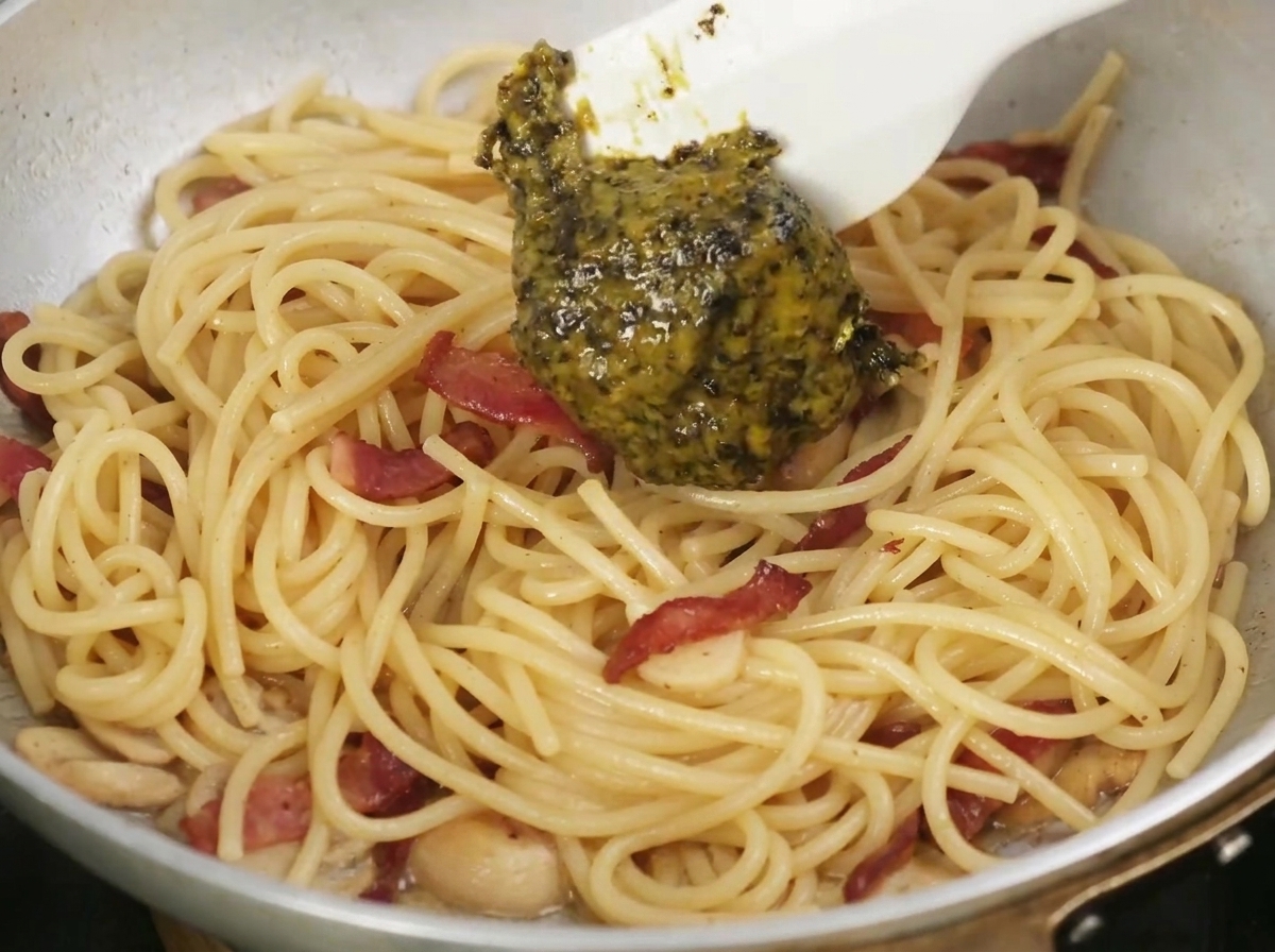 Sauce à la truffe noire versée à la cuillère dans une poêle de pâtes cuites et de bacon.