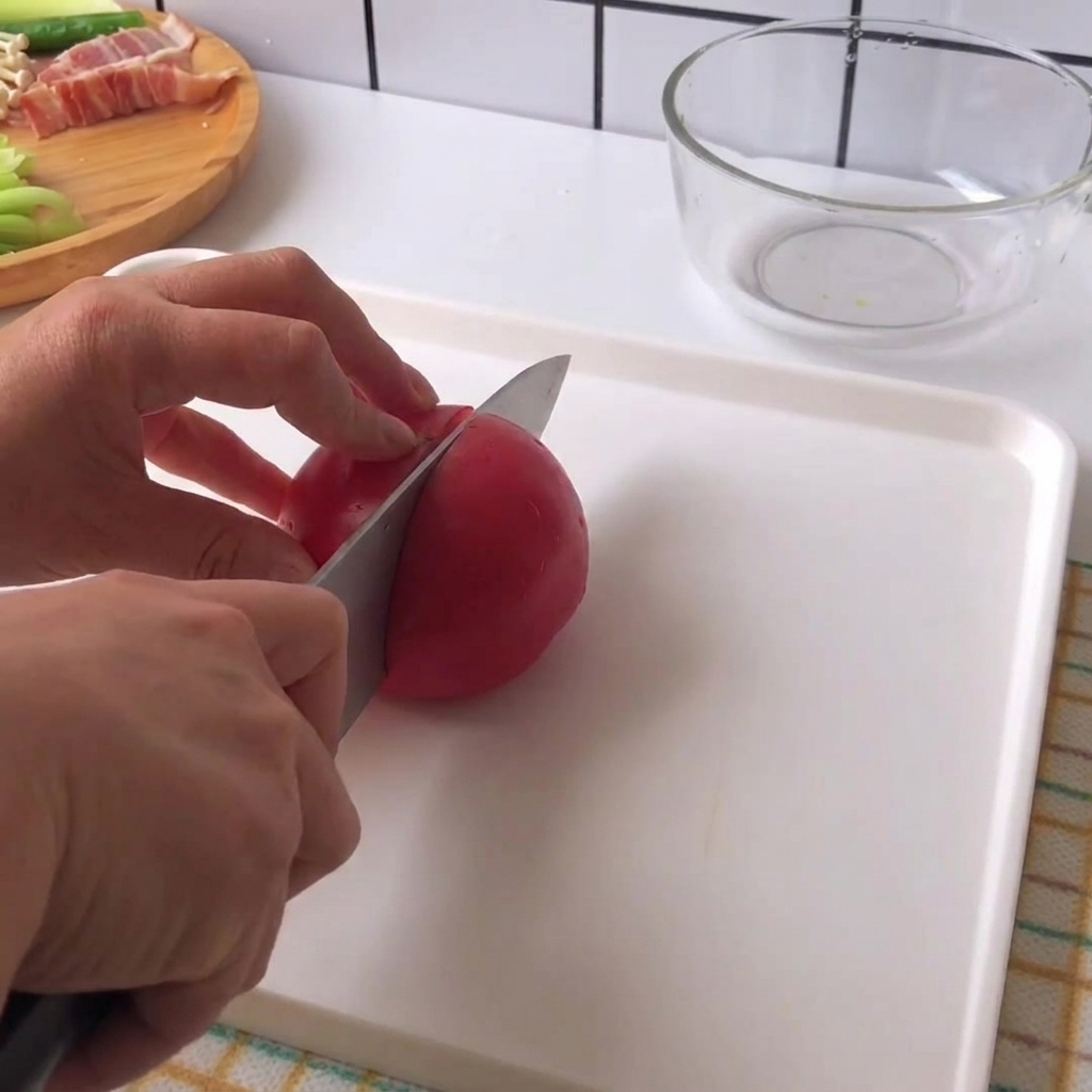 Mains tenant un couteau et tranchant une tomate rouge fraîche en morceaux sur une planche à découper blanche.