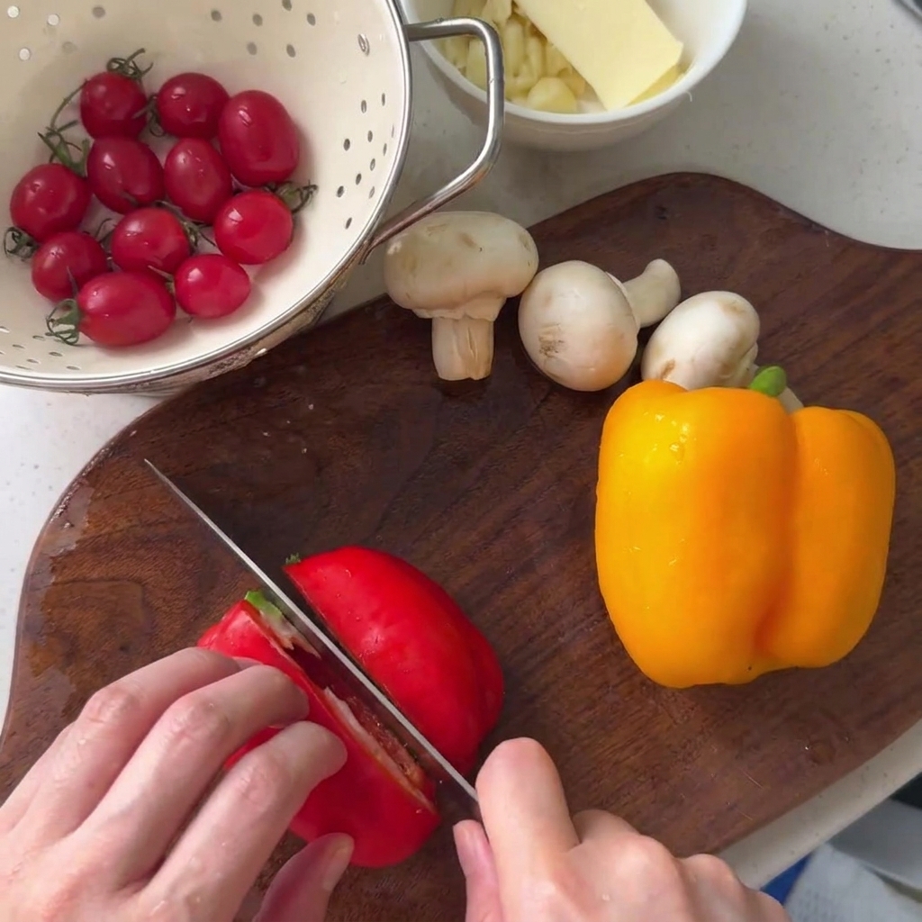 Un poivron rouge en cours de découpe sur une planche à découper en bois à côté dun poivron jaune et de champignons de Paris.