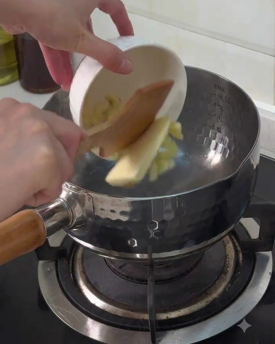 De lail émincé et un morceau de beurre versés dun petit bol blanc dans une casserole en métal sur la cuisinière.