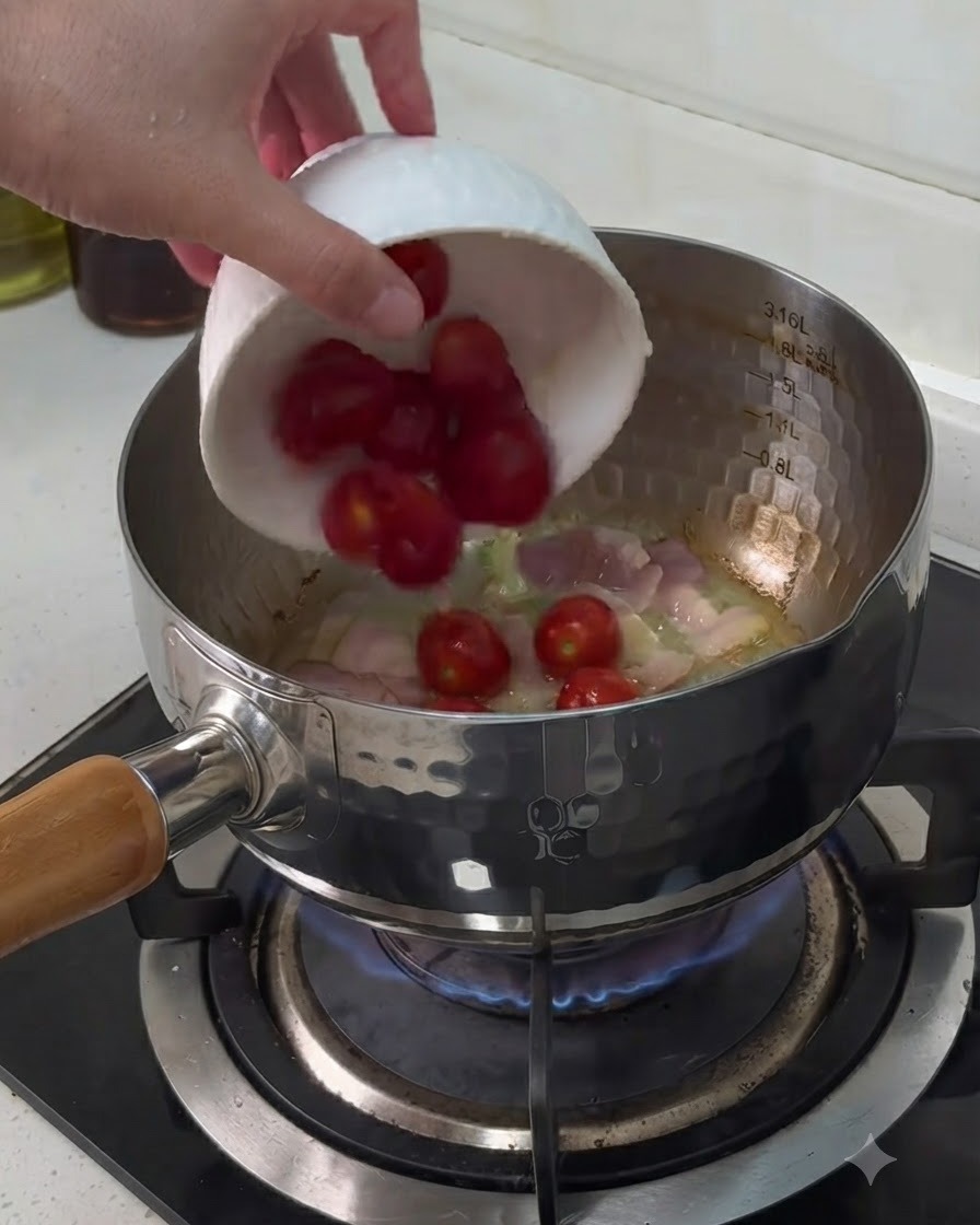Des tomates cerises ajoutées dun petit bol blanc dans une casserole contenant des morceaux de bacon en cours de cuisson.