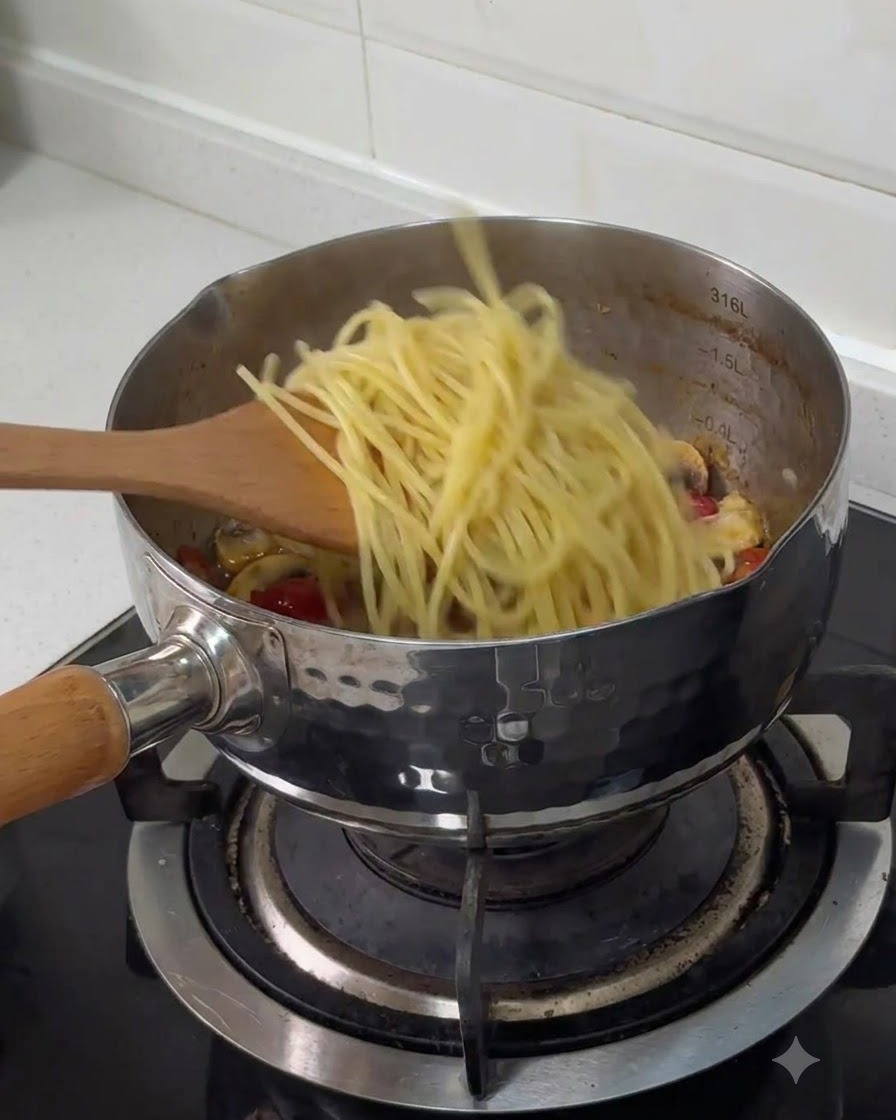Des spaghettis bouillis transférés dune spatule en bois vers une casserole en acier inoxydable avec dautres ingrédients cuits.