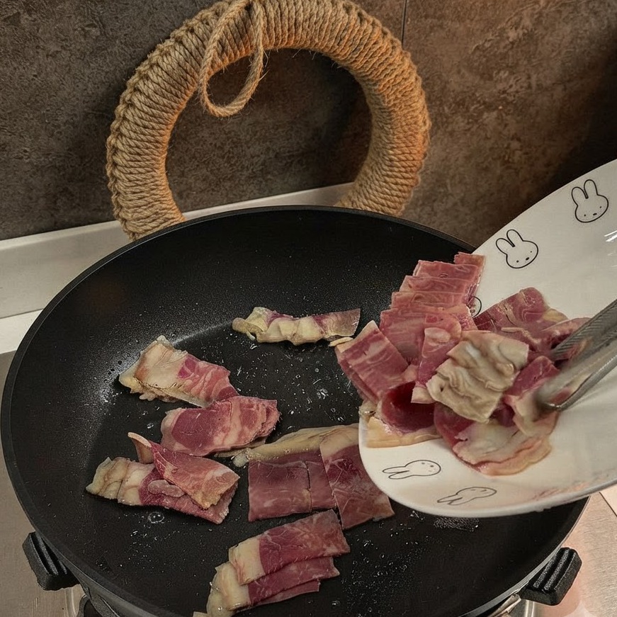 Morceaux de bacon tranchés en train de rissoler dans une poêle noire.