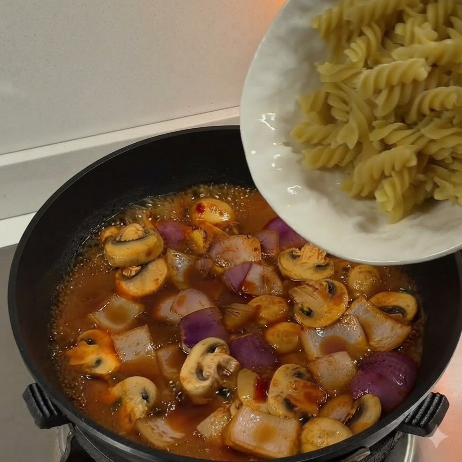 Pâtes fusilli bouillies versées depuis une assiette blanche dans une poêle remplie de sauce frémissante et de légumes.