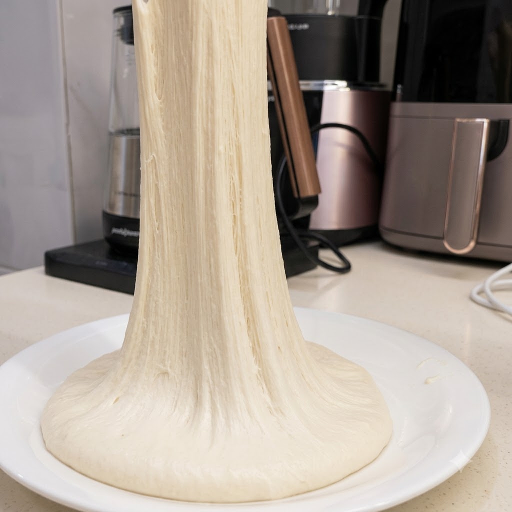 Un long brin continu de pâte à pizza très élastique étiré vers le haut depuis une assiette blanche.