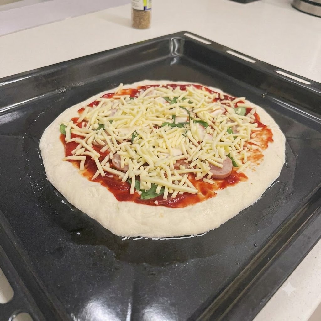 Une pizza crue garnie de sauce tomate, de tranches de saucisse, de basilic frais et de fromage râpé sur une plaque de cuisson noire.