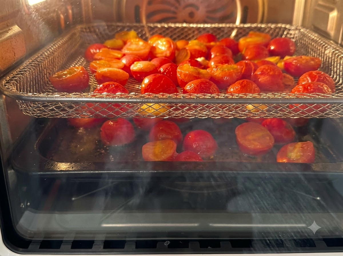 Des tomates cerises coupées en deux disposées sur des grilles de friteuse à air en train de cuire à lintérieur de lappareil.