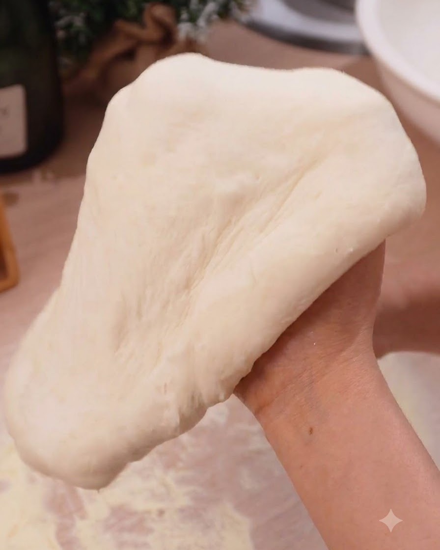 De la pâte à pizza étirée en douceur sur des mains fermées dans un cadre de cuisine.
