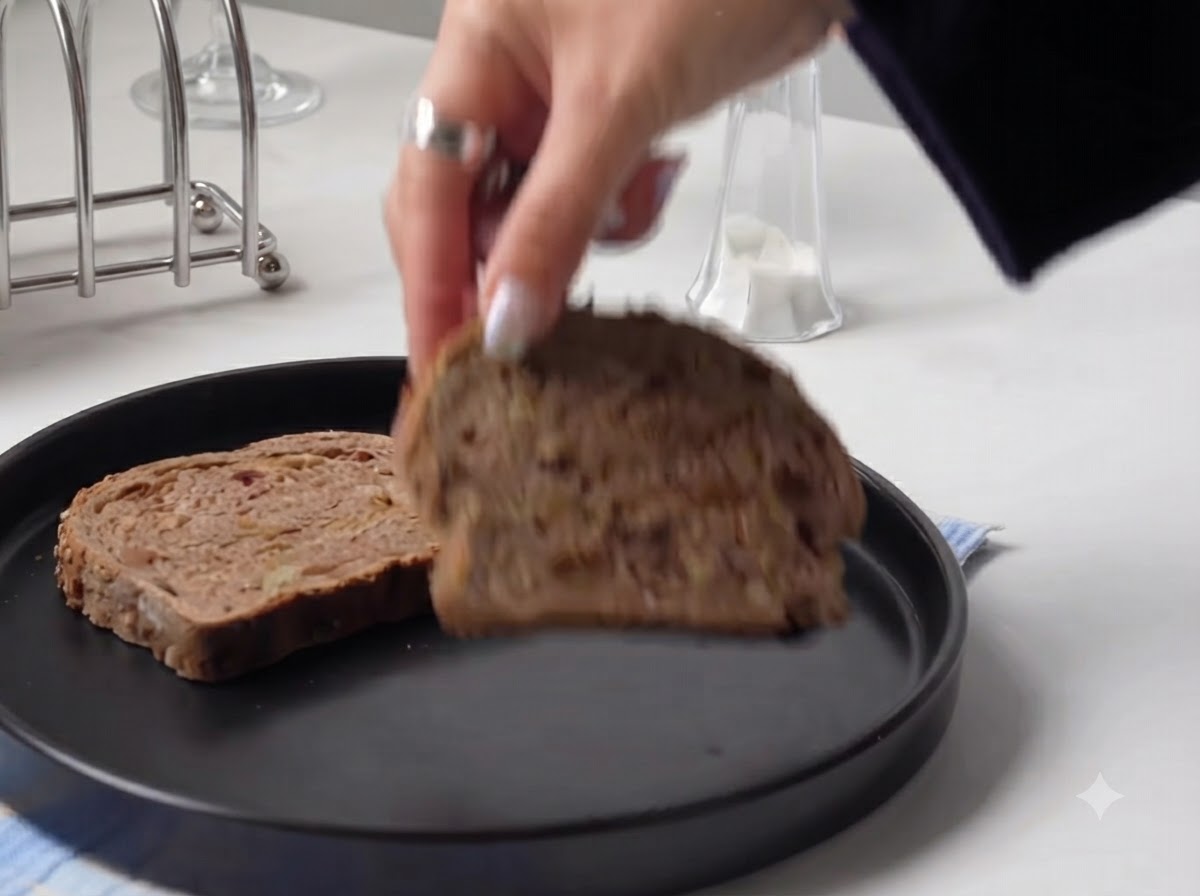 Une main posant une tranche épaisse de pain rustique sur une assiette ronde noire.