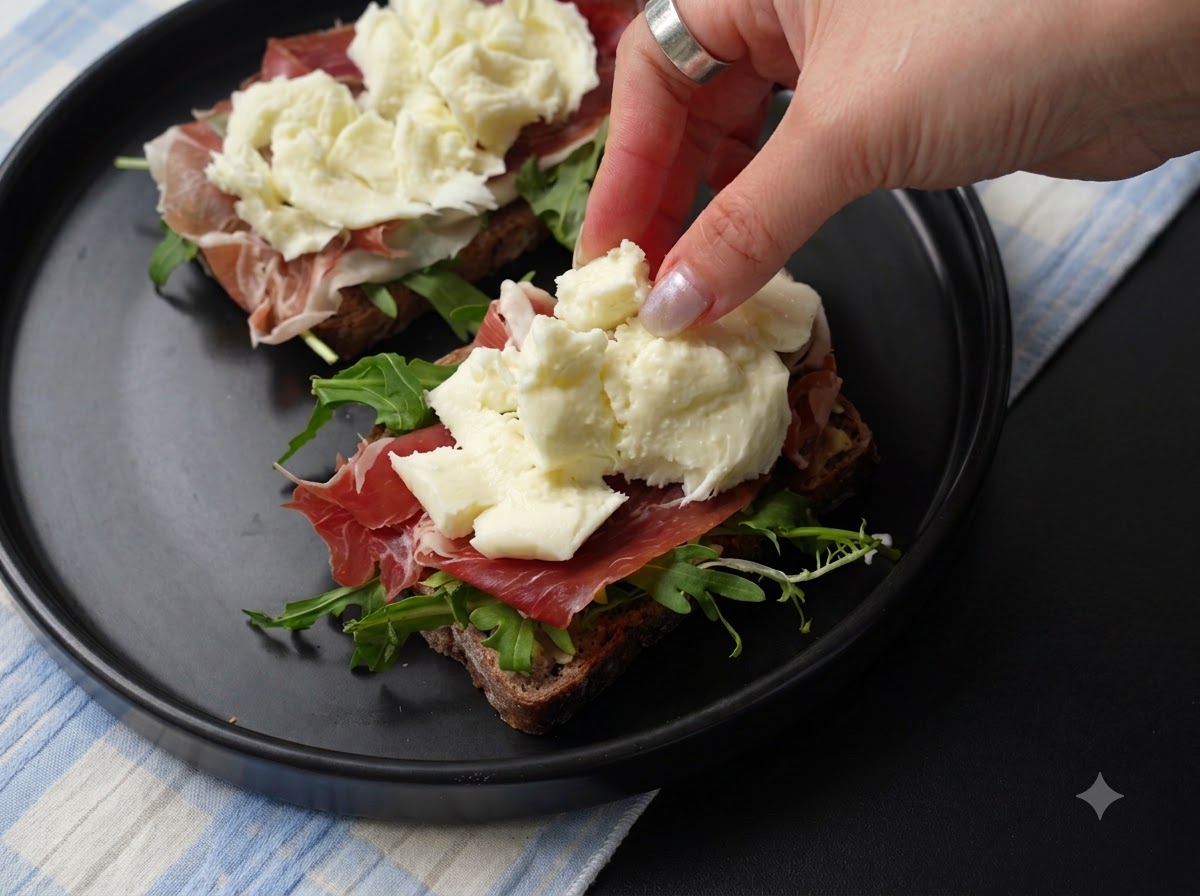 Des morceaux frais de mozzarella déchirée placés sur la couche de jambon de la tartine.