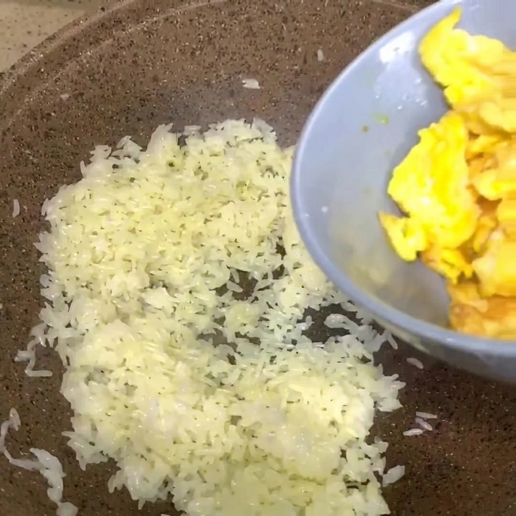 Œufs brouillés provenant dun bol gris versés dans une poêle de riz blanc cuit.