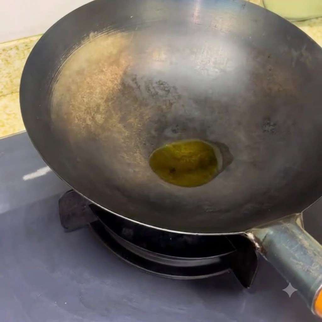 Un wok noir posé sur un brûleur de cuisinière avec une petite quantité dhuile en train de chauffer à lintérieur.