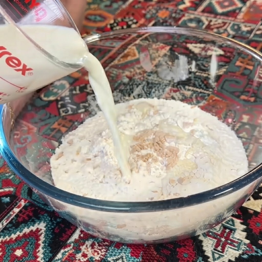 Du lait versé dune tasse à mesurer en verre transparent dans un bol de farine et de levure.