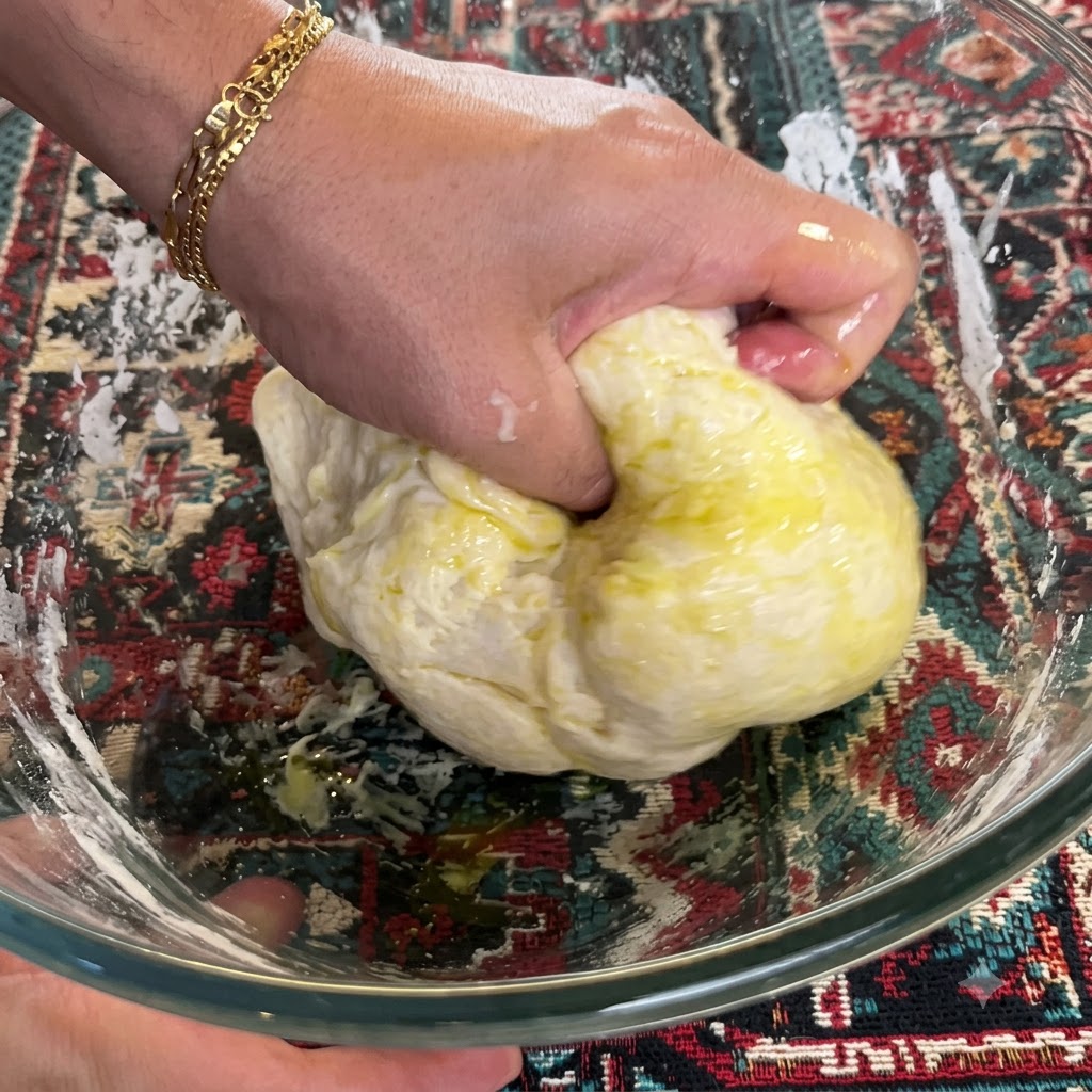 Une main pétrissant et pliant fermement la pâte mélangée avec de lhuile dolive à lintérieur dun bol en verre.