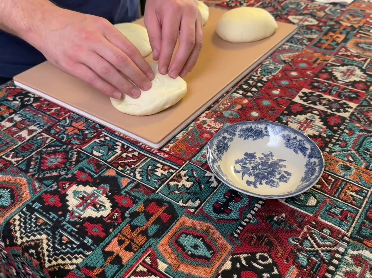 Des mains pressant et aplatissant une boule ronde de pâte à pizza sur une planche en bois.