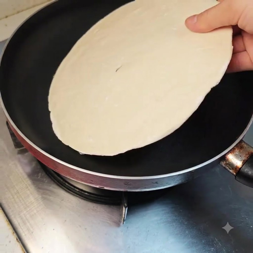Une crêpe à la ciboule posée à plat dans une poêle antiadhésive propre sur une cuisinière éteinte.