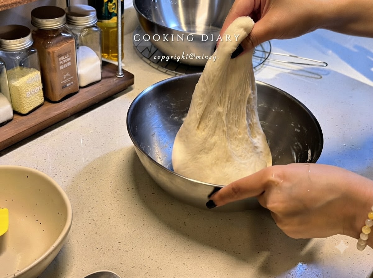 Une paire de mains soulevant vers le haut une portion de pâte à pizza élastique à lintérieur dun bol en métal pour létirer.