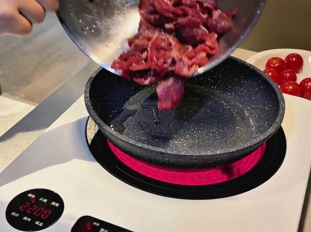 Des tranches de bœuf marinées crues versées dun bol en métal dans une poêle chaude tachetée sur une plaque à induction.