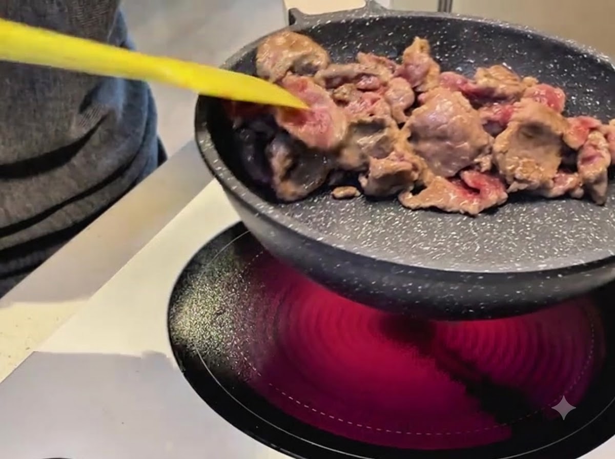 Utilisation dune spatule jaune pour faire sauter des tranches de bœuf dans une poêle antiadhésive sur une cuisinière électrique.