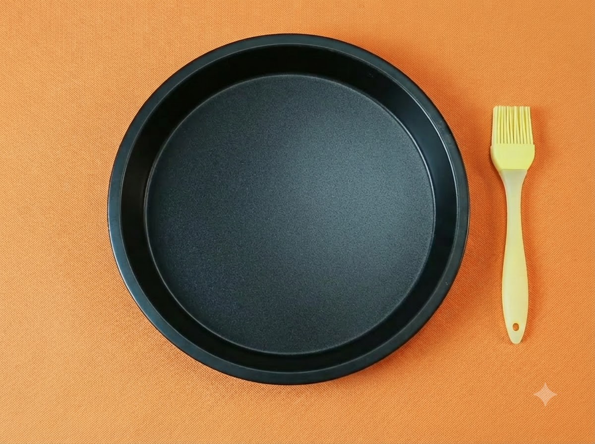 Un moule a pizza rond noir vide associe a un pinceau a huile en silicone jaune sur fond orange.