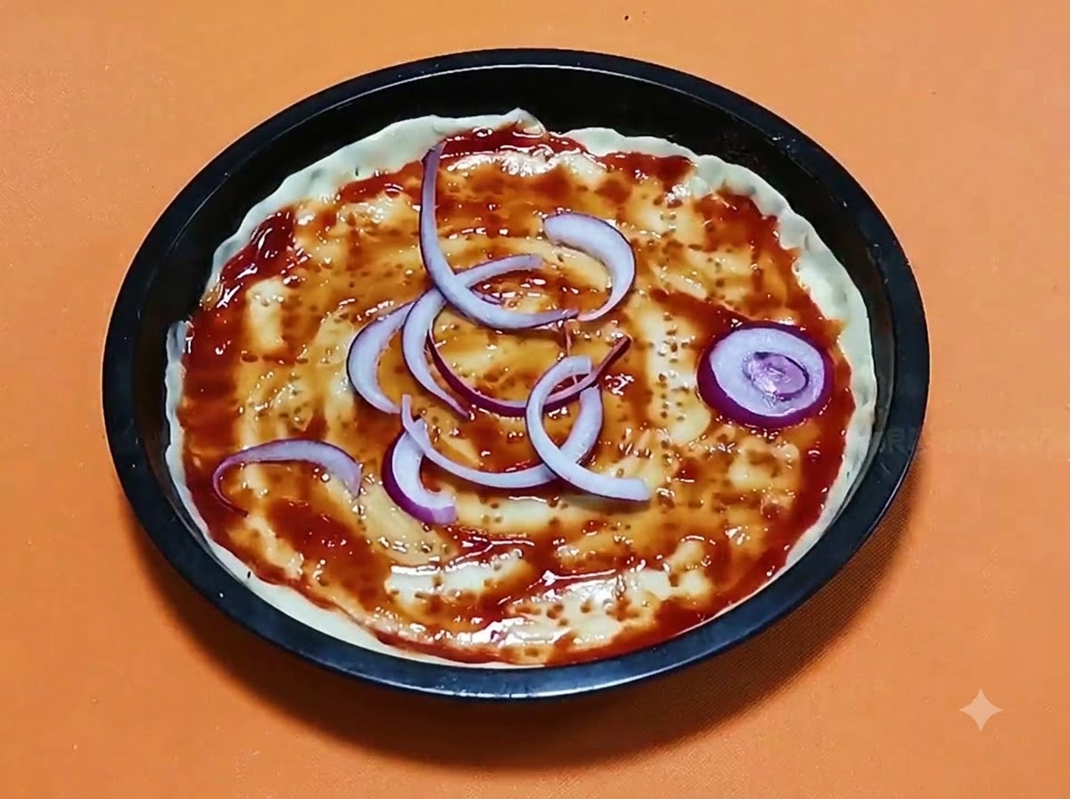 Des anneaux doignon rouge disposes sur une base de pate a pizza saucee dans un moule de cuisson rond noir.