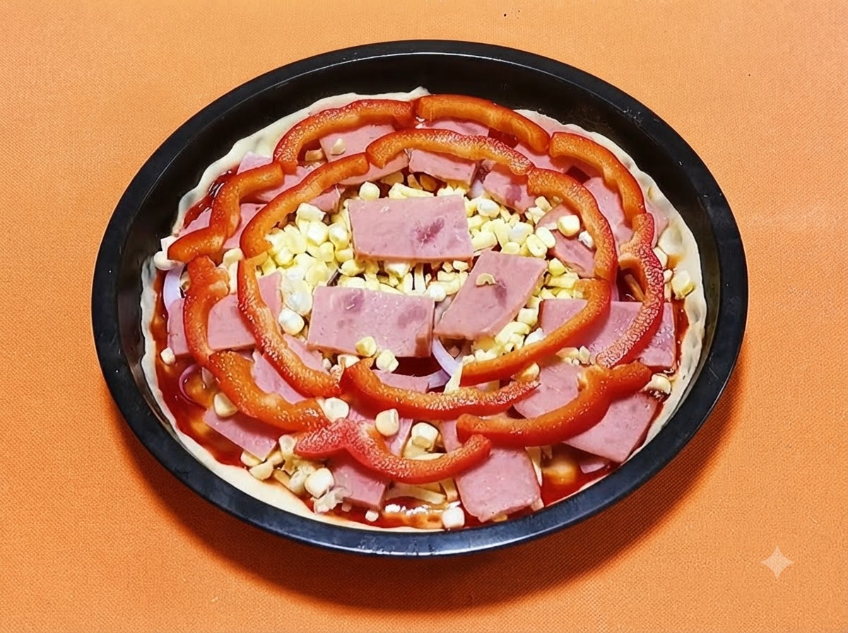 Croute de pizza dans un moule noir garnie de sauce, de jambon, de grains de mais jaune et de tranches de poivron rouge.