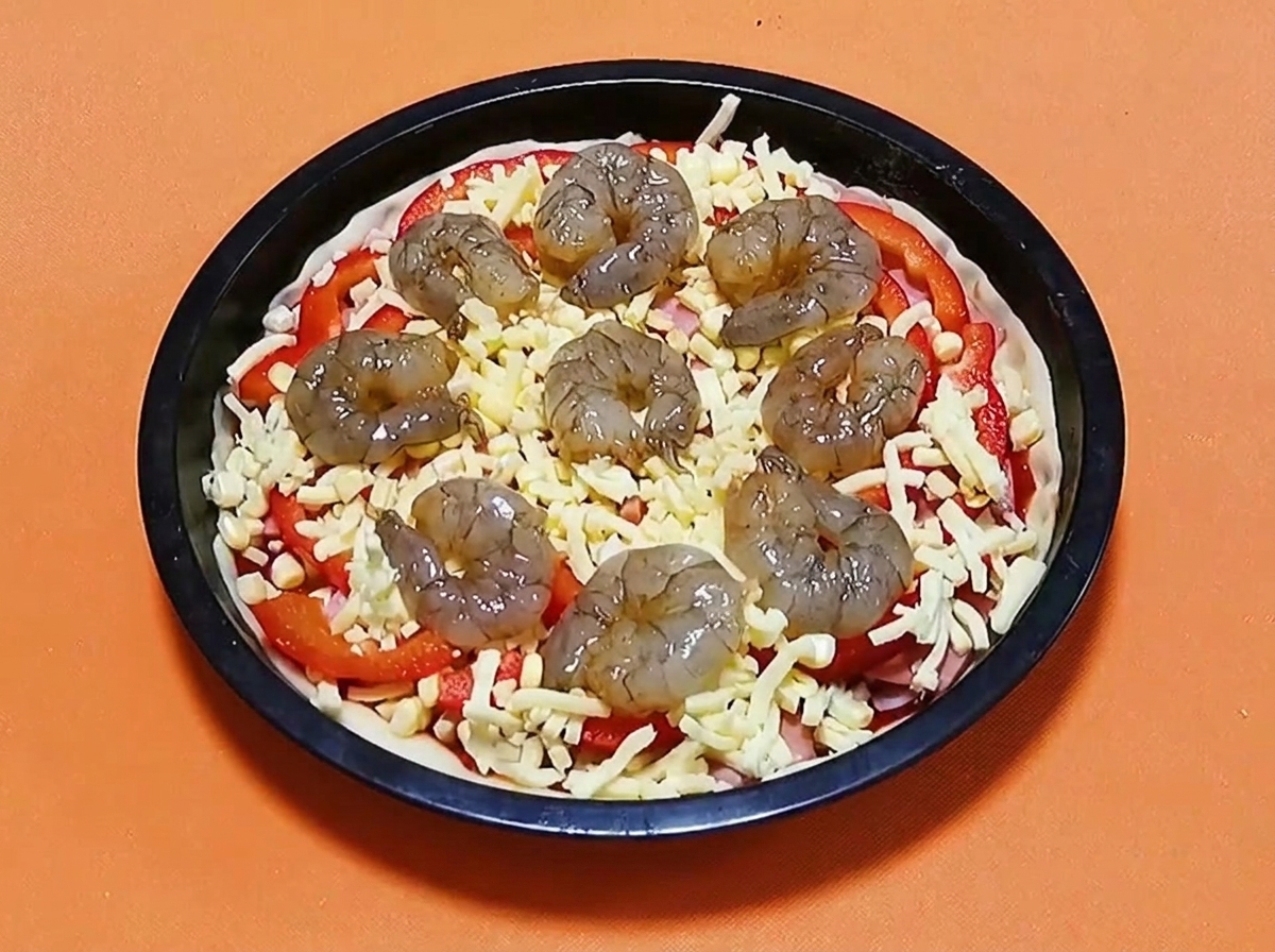 Crevettes crues marinees disposees en cercle sur le dessus dune pizza au fromage, poivrons et jambon.
