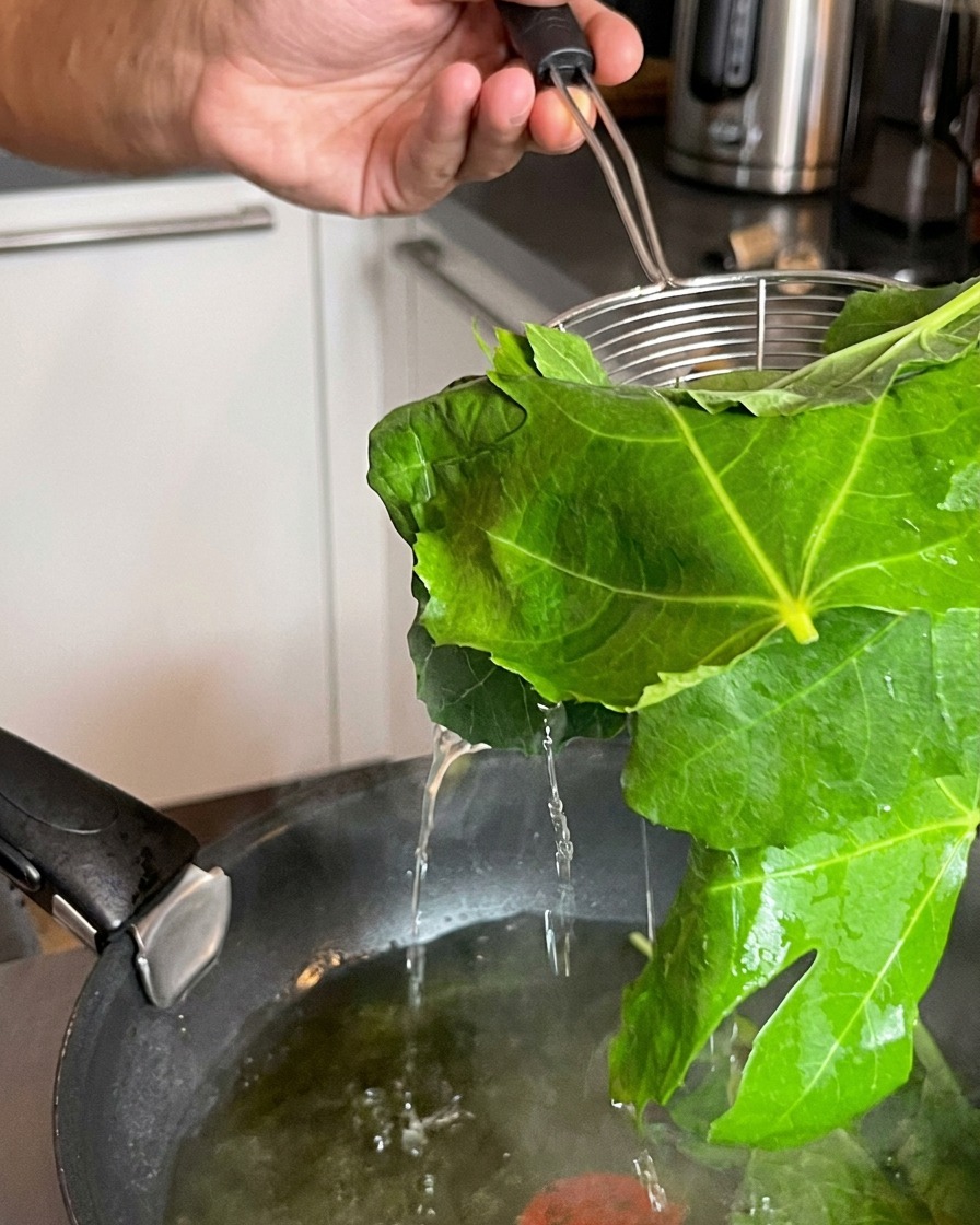 Une écumoire extrayant des feuilles vertes fraîchement blanchies dune casserole deau bouillante.