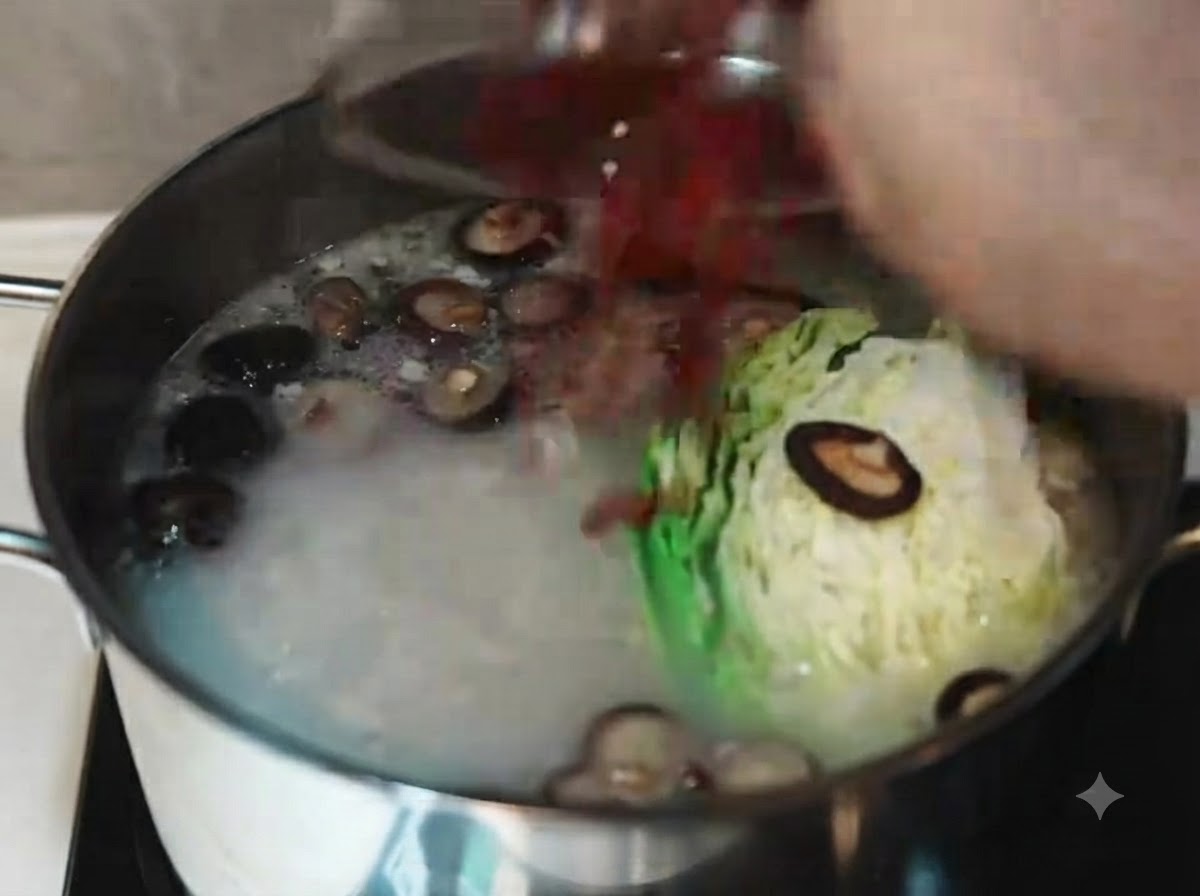 Remuer un bouillon de porc bouillant et opaque avec une louche blanche après y avoir incorporé du chou, des rondelles de carotte, des champignons shiitake et des baies de goji.