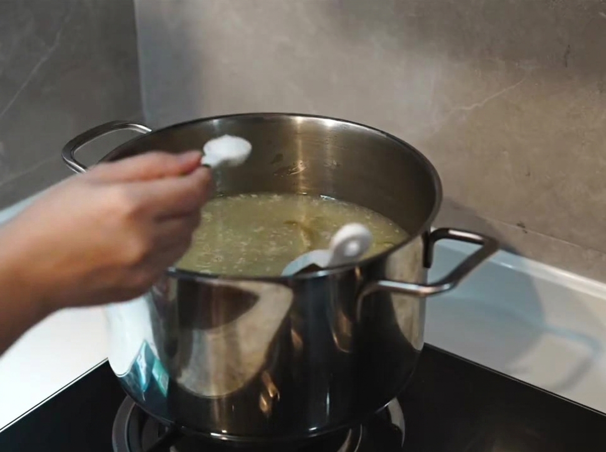 Une cuillerée de sel ajoutée à une soupe de couleur blanc laiteux, épaissie et frémissante dans une marmite en inox.