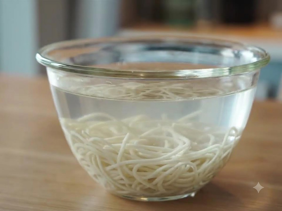 Nouilles ramen fraîchement cuites, submergées et refroidissant dans un bol en verre rempli deau froide après le rinçage.