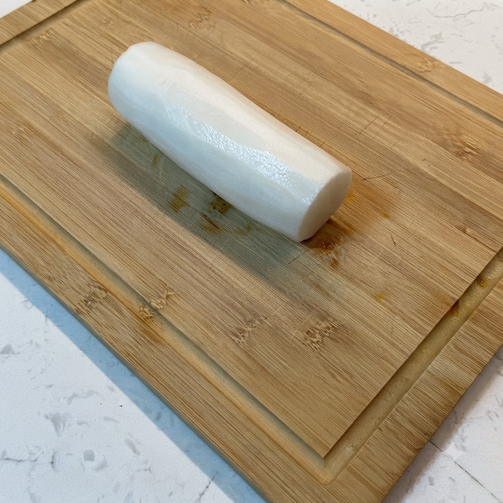 Un radis blanc coupé en fines lanières sur une planche à découper en bois.