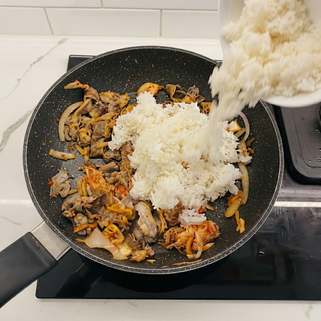 Riz blanc versé dun bol dans la poêle contenant le bœuf et le kimchi.