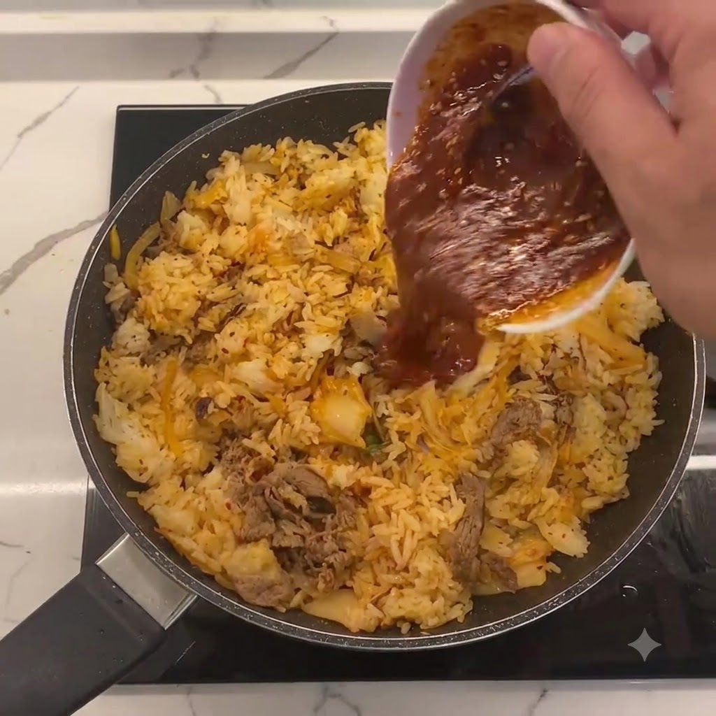 Sauce spéciale versée dun petit bol blanc au centre de la poêle contenant le riz sauté, le kimchi et le bœuf.