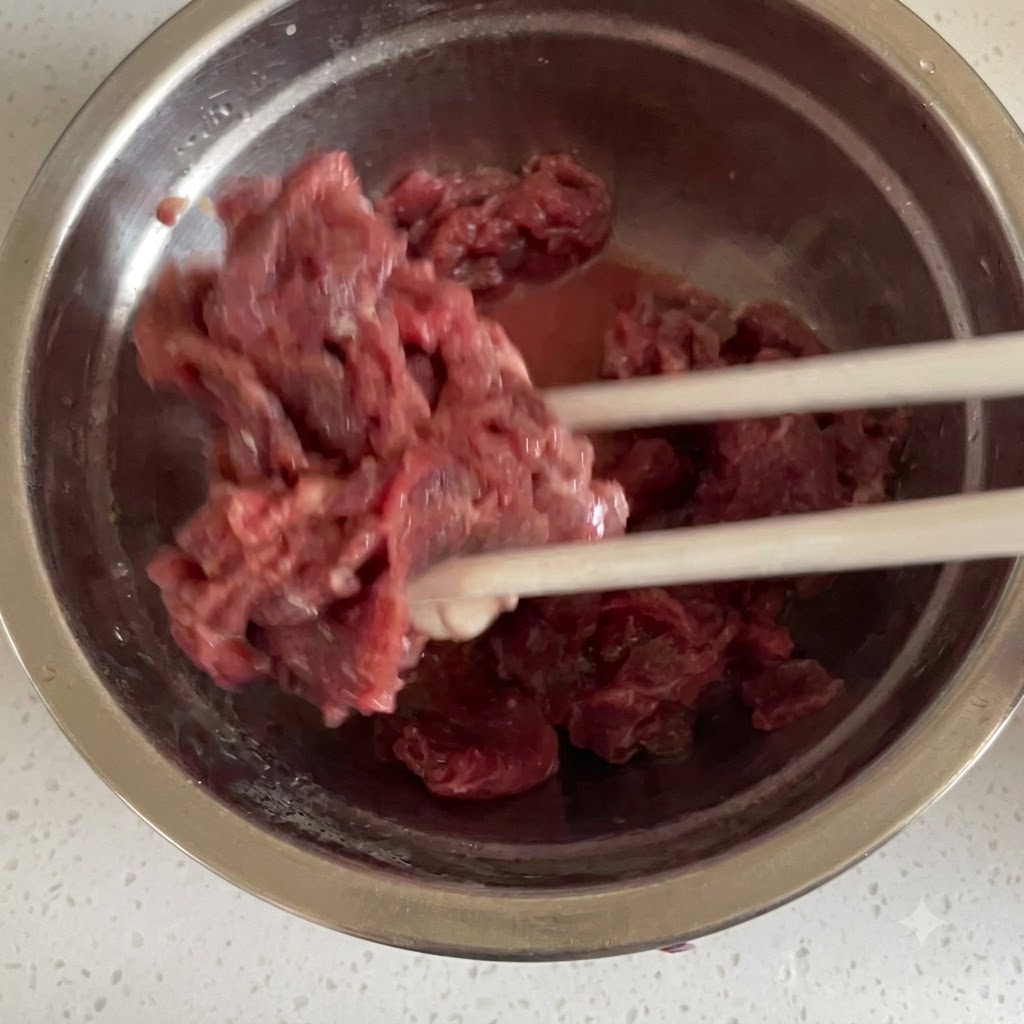 Du bœuf cru coupé en fines tranches mélangé avec les ingrédients de la marinade à laide de baguettes dans un bol en acier inoxydable.