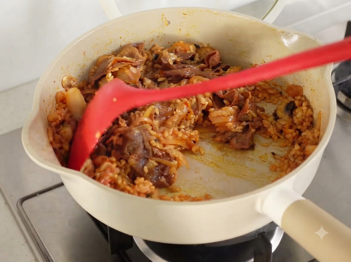 Tous les ingrédients et le riz bien sautés ensemble jusquà être enrobés de jus de kimchi dans une poêle.