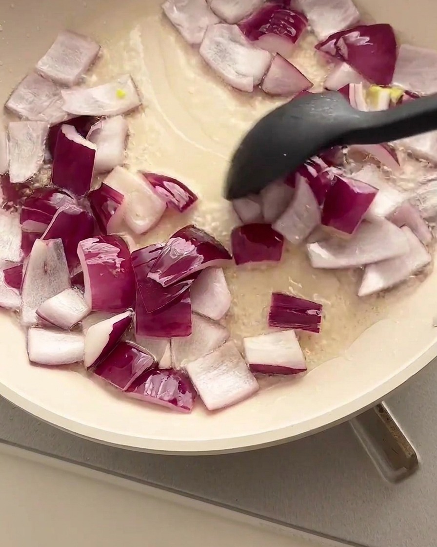 Dés doignons rouges sautés dans une poêle huilée avec une spatule noire.