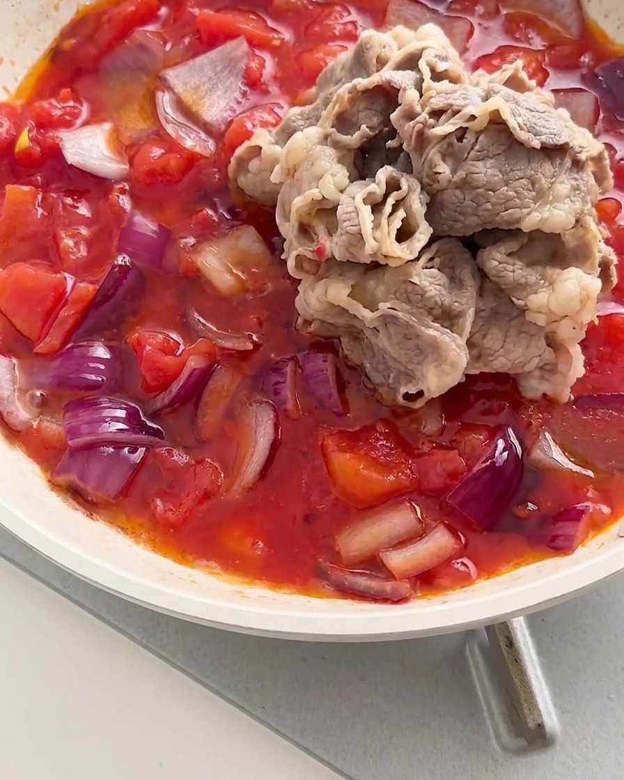 Tas de fines tranches de bœuf ajouté dans la poêle avec le mélange de tomates et doignons frémissant.