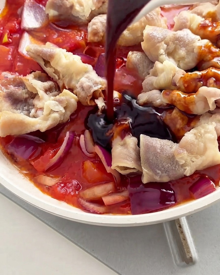 Sauce foncée versée sur le bœuf et les tomates à lintérieur dune poêle blanche.