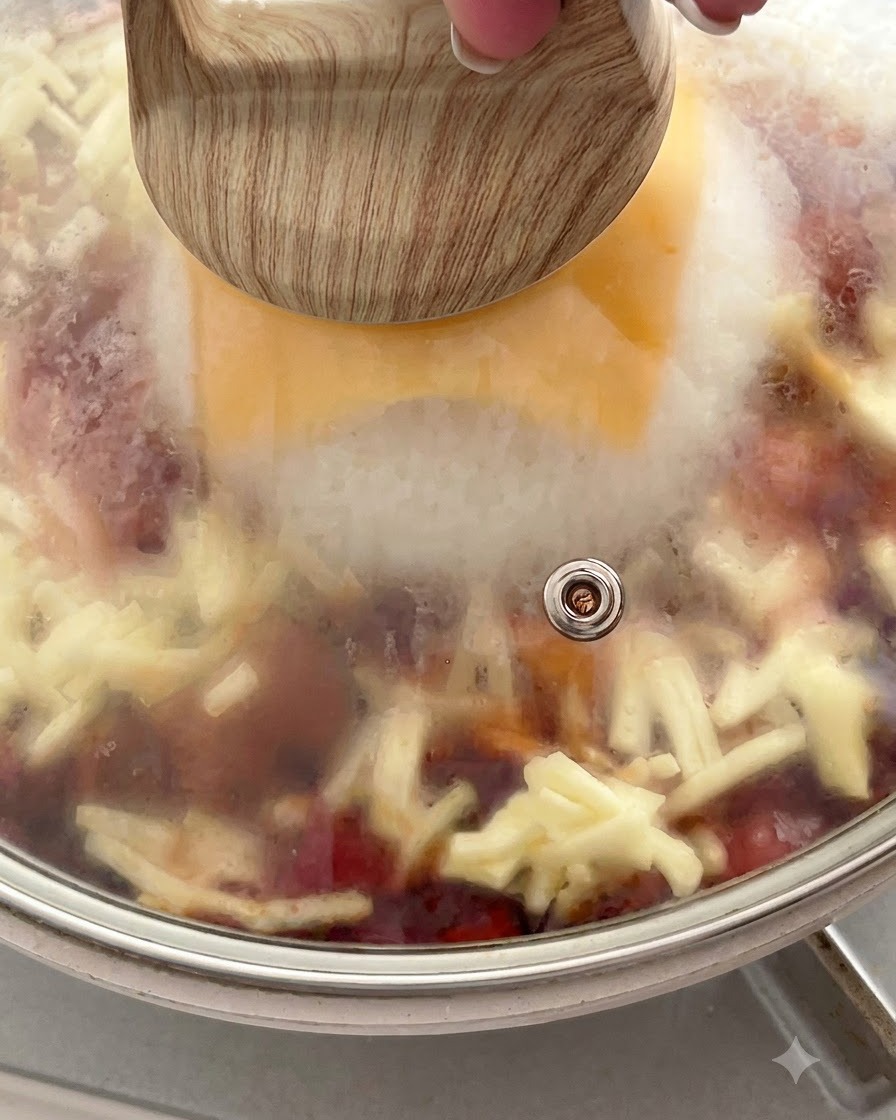 Poêle couverte dun couvercle en verre retenant la vapeur au-dessus du fromage fondu et du riz.