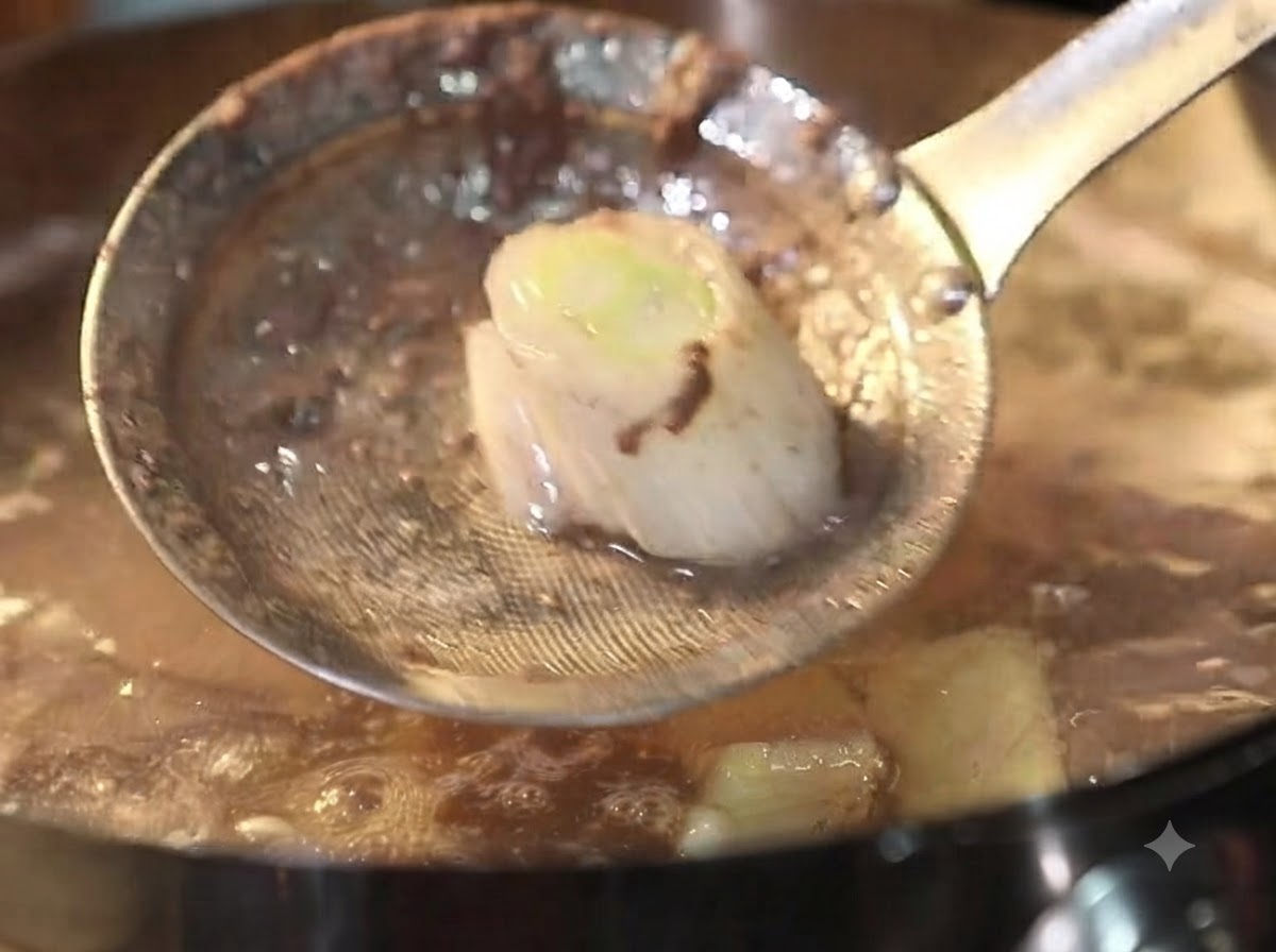 Une écumoire en métal retirant la mousse et les débris dun bouillon de bœuf frémissant.
