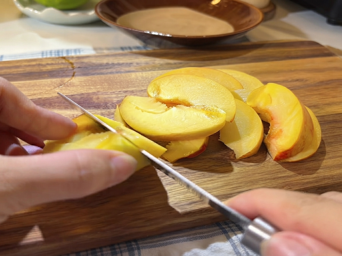 Une main utilisant un petit couteau pour trancher des moitiés de pêche jaune fraîche en fines tranches sur une planche à découper en bois.