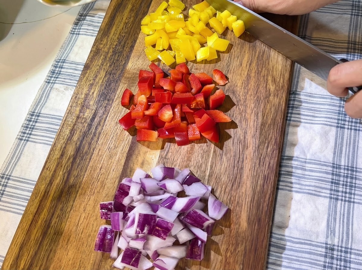 Des tas de poivrons rouges et jaunes fraîchement coupés et des oignons rouges émincés disposés soigneusement sur une planche à découper en bois.