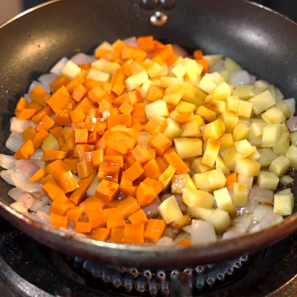 De la sauce soja foncée versée sur des carottes et des pommes de terre en dés dans une poêle.