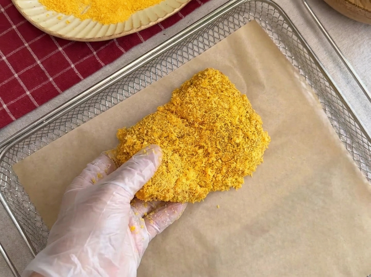 Une côtelette de porc panée placée délicatement sur une grille recouverte de papier sulfurisé.