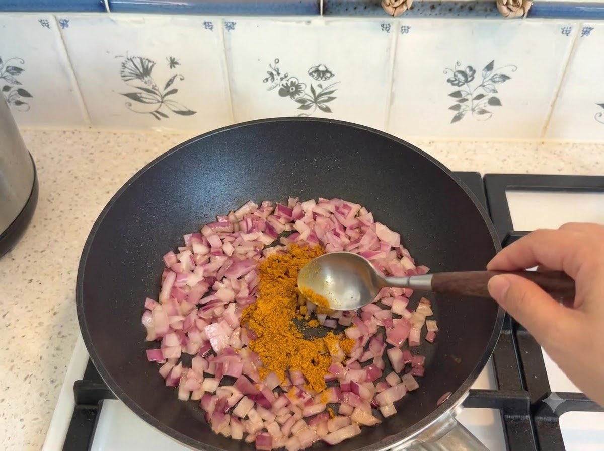 De la poudre de curry mesurée à laide dune cuillère et ajoutée aux oignons sautés dans une poêle.