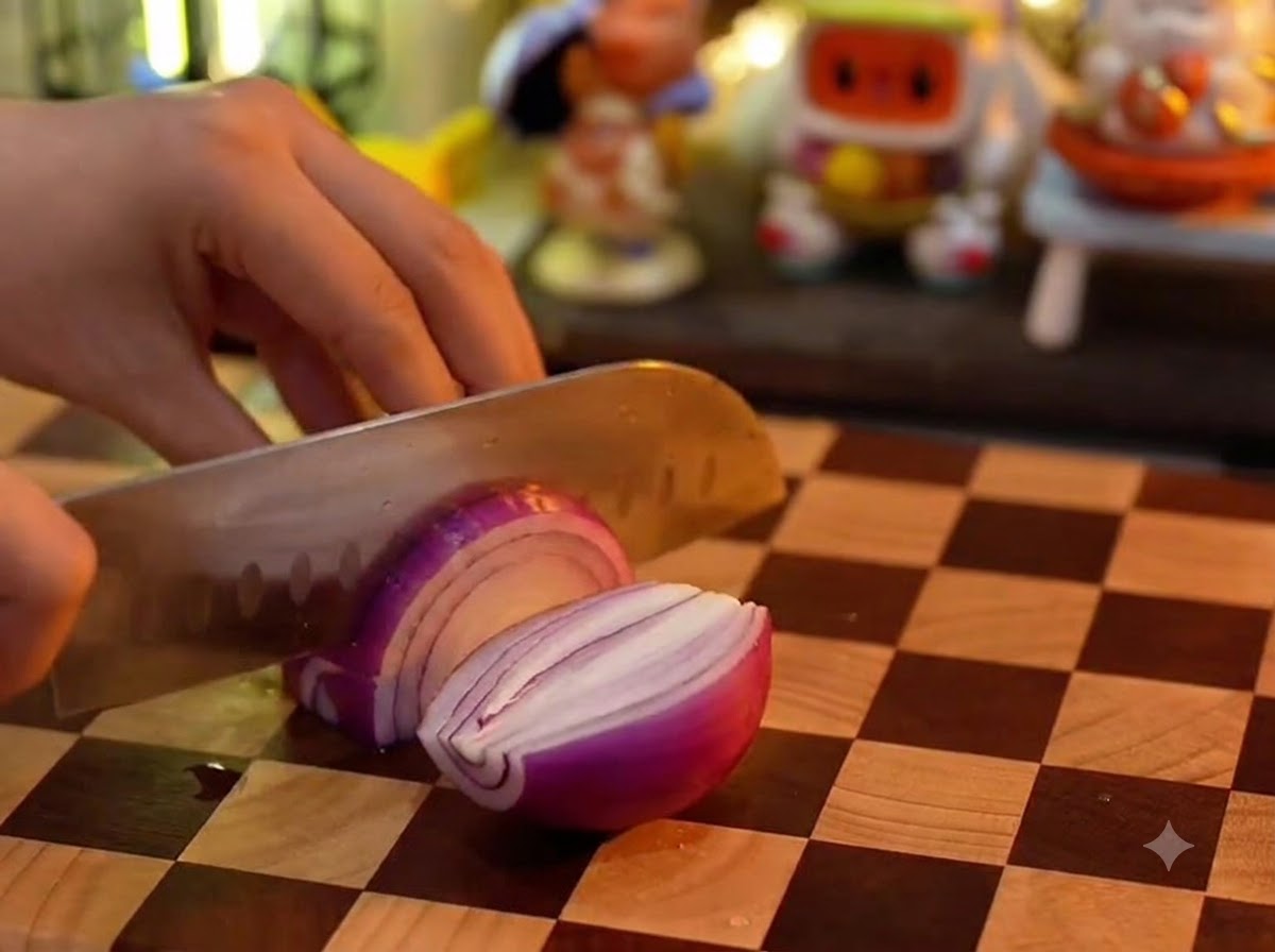 Un couteau de cuisine tranchant un oignon rouge sur une planche à découper à damier en bois.